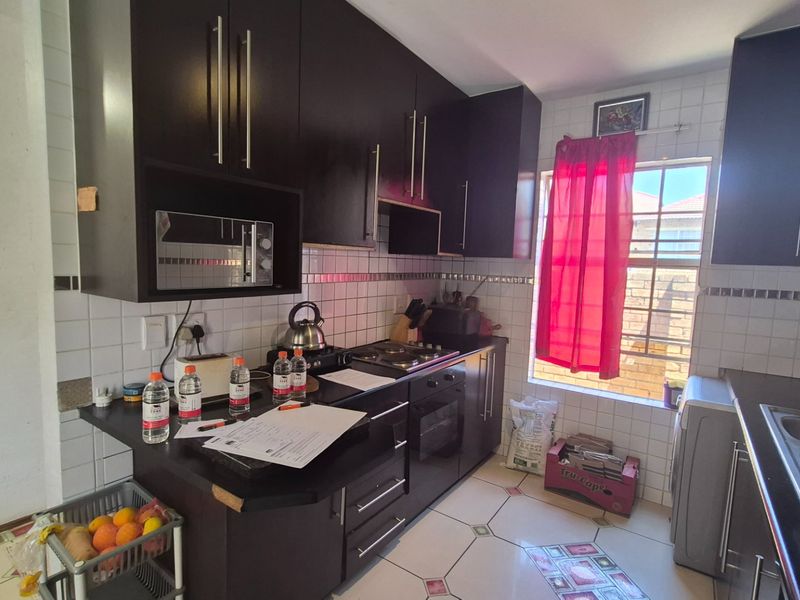 A functional kitchen featuring dark cabinetry, built-in appliances including an oven and hob, tiled backsplash, and a window providing natural light.