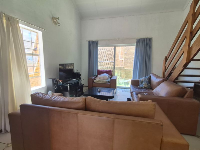 Spacious living room featuring a vaulted ceiling, tiled flooring, and a wooden staircase leading to an upper level, with access to an outdoor area.