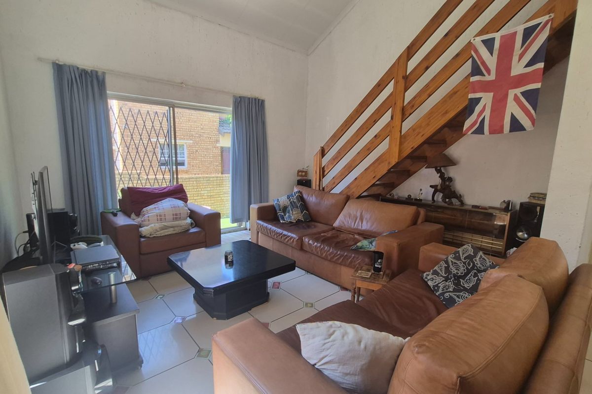 Spacious living room featuring a wooden staircase, tiled flooring, and a sliding glass door providing access to the exterior.