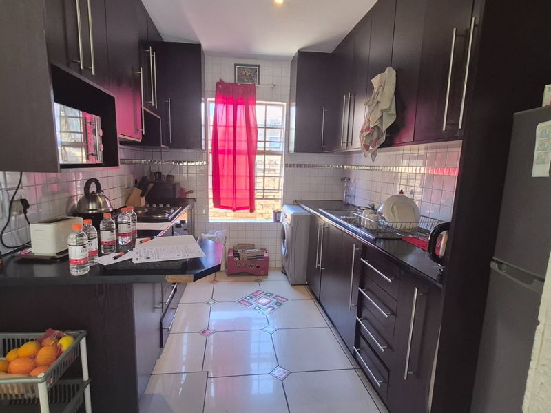 A functional galley-style kitchen featuring dark cabinetry, tiled backsplash, and tiled flooring with a window providing natural light.