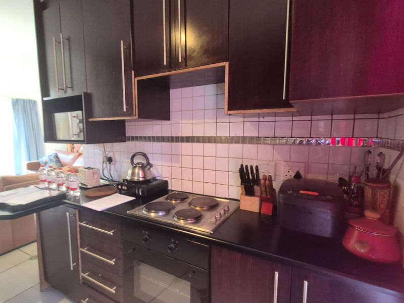 Compact kitchen featuring dark wood-finish cabinetry, a built-in electric oven and hob, and a tiled backsplash, offering functional storage and preparation space.