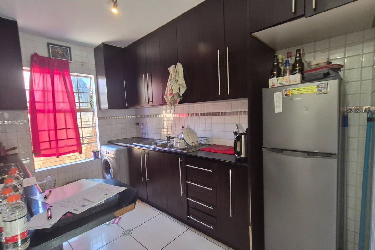 A functional kitchen featuring dark wood cabinetry, tiled backsplash, and tiled flooring, providing a practical workspace with integrated storage and sink area.