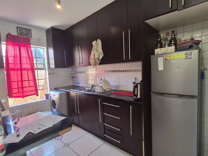 A functional kitchen featuring dark wood cabinetry, tiled backsplash, and tiled flooring, providing a practical workspace with integrated storage and sink area.
