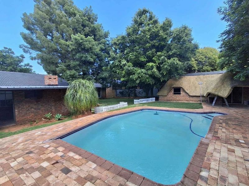 Outdoor pool area featuring brick paving, a swimming pool, and a secondary building with a traditional thatched roof set in a garden.