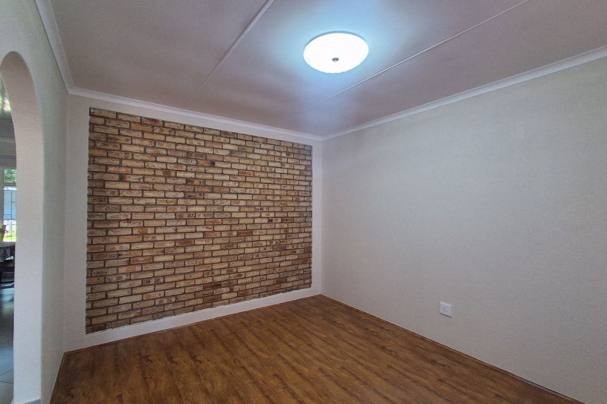 A bright, empty living room featuring a rustic exposed brick accent wall and warm-toned laminate flooring, offering a clean canvas for interior design.