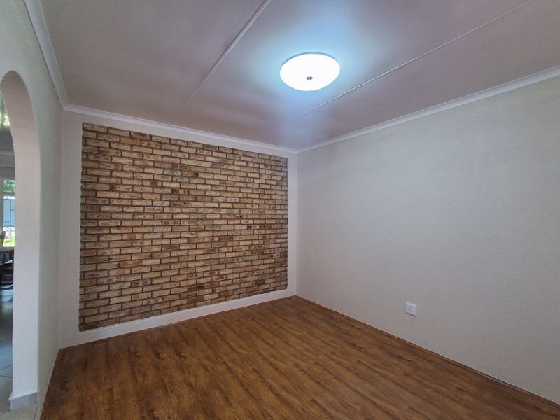 A bright, empty living room featuring a rustic exposed brick accent wall and warm-toned laminate flooring, offering a clean canvas for interior design.