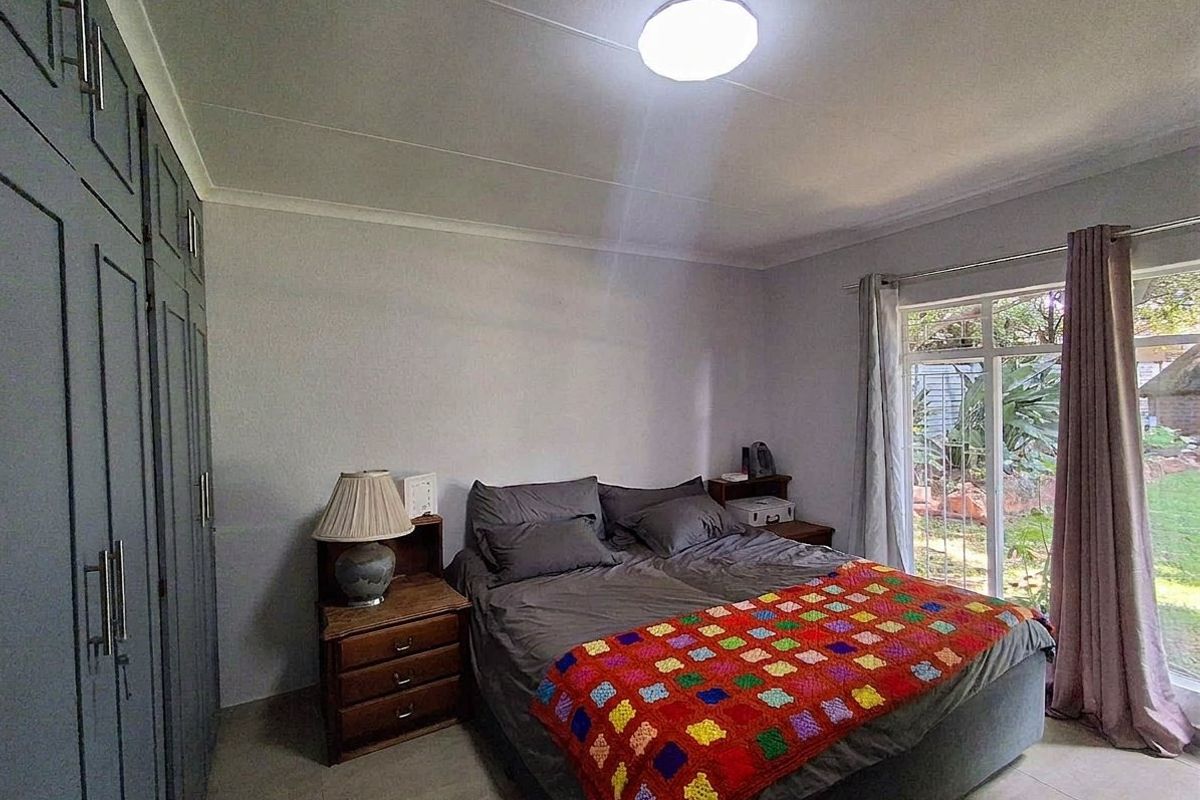 A well-maintained bedroom featuring built-in cupboards, tiled flooring, and a sliding glass door providing direct access to the garden.