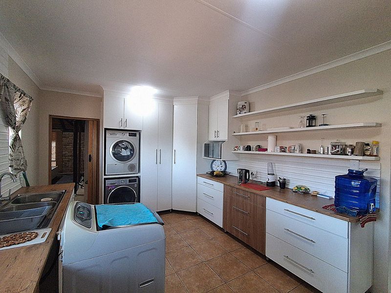 A functional laundry room featuring built-in cabinetry, laminate countertops, a double basin sink, and open shelving for storage.