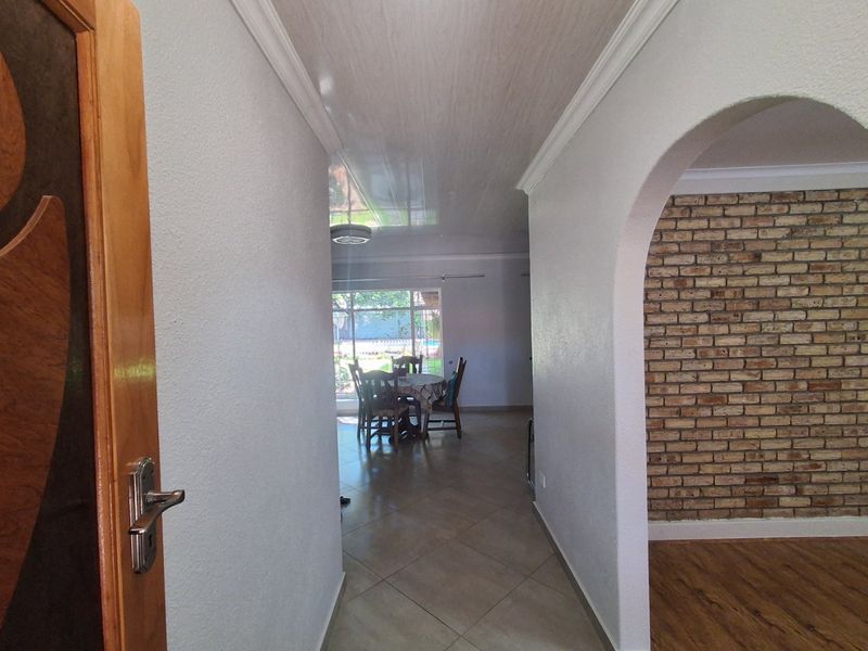 A bright hallway featuring an arched entryway, exposed brick feature wall, and a transition between tiled and laminate flooring leading into the living area.
