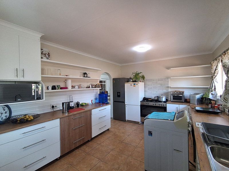 A functional kitchen featuring wooden countertops, white and wood-tone cabinetry, open shelving, and built-in cooking appliances with tiled flooring.