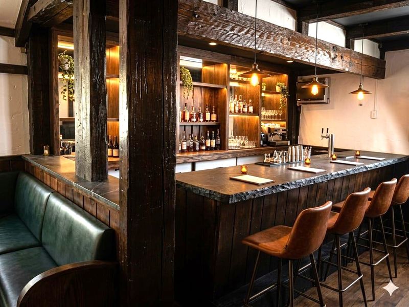 A sophisticated, rustic-style bar area featuring exposed timber beams, a stone-topped counter, and custom built-in shelving with integrated ambient lighting.