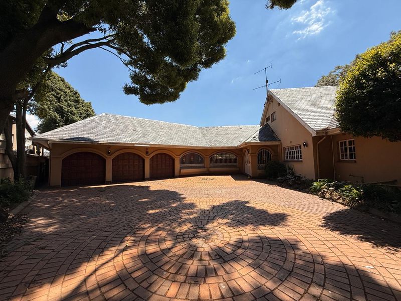 Spacious front exterior featuring a large circular paved driveway, triple garage with arched doors, and a well-maintained tiled roof facade.