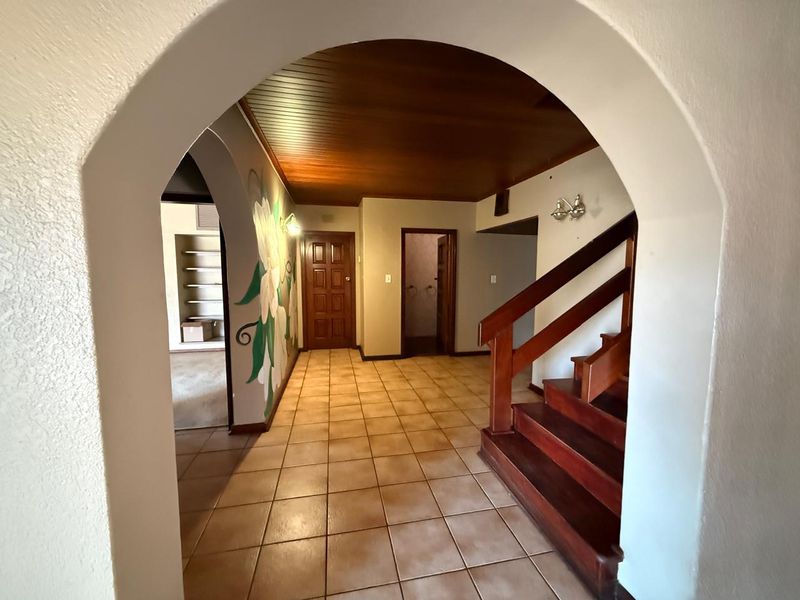 Spacious entrance hall featuring an arched entryway, a timber-clad ceiling, tiled flooring, and a classic wooden staircase leading to the upper level.