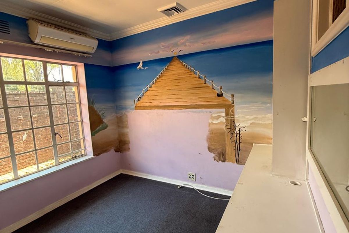 A vacant bedroom featuring a built-in vanity, split-system air conditioning, and carpet flooring, currently decorated with a large wall mural.