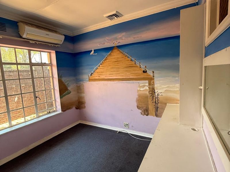 A vacant bedroom featuring a built-in vanity, split-system air conditioning, and carpet flooring, currently decorated with a large wall mural.