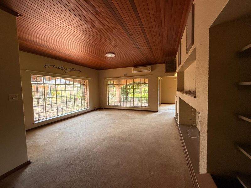 Spacious living room featuring a timber ceiling, split-system air conditioning, and built-in shelving, offering a blank canvas for potential updates.