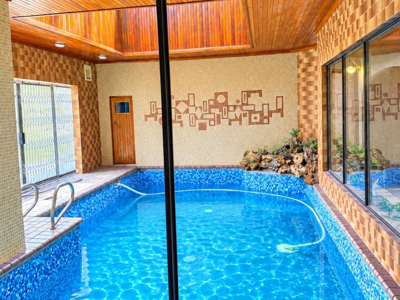 An indoor swimming pool area featuring a timber-paneled ceiling with a skylight, mosaic tiling, and decorative wall finishes, creating a bright and enclosed leisure space.