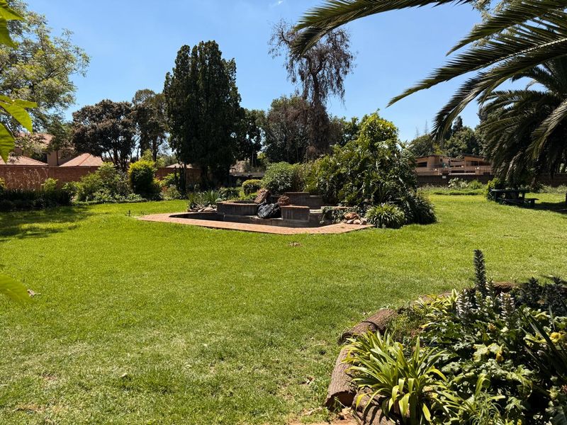 A spacious, established garden featuring a central brick-edged water feature, mature trees, and expansive lawn areas, offering a private outdoor setting.