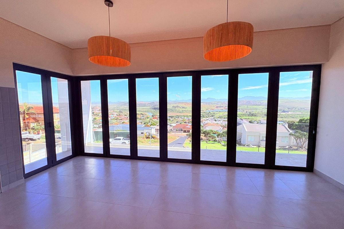Spacious living area featuring large format floor tiles and expansive black aluminium stacker doors that open to panoramic neighbourhood and landscape views.
