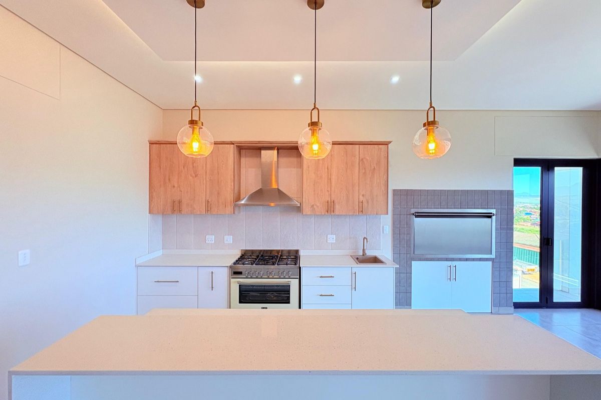 Modern kitchen featuring light wood cabinetry, stone countertops, gas stove, built-in oven, and an integrated indoor braai area with sleek pendant lighting.