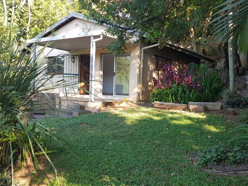 Rear view of the property featuring a covered patio, sliding glass doors, and a landscaped garden area set against a natural backdrop.