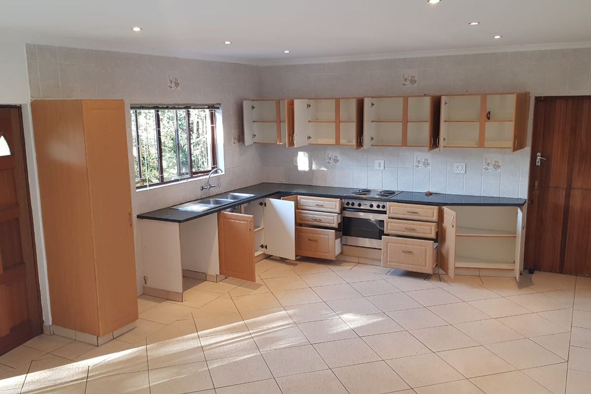 A spacious, empty kitchen featuring built-in cabinetry, a stainless steel sink, and a built-in oven with an electric hob.