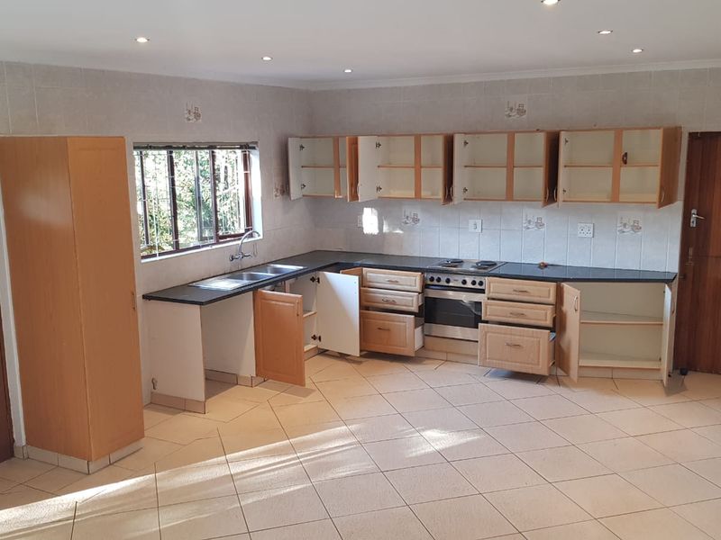 A spacious, empty kitchen featuring built-in cabinetry, a stainless steel sink, and a built-in oven with an electric hob.