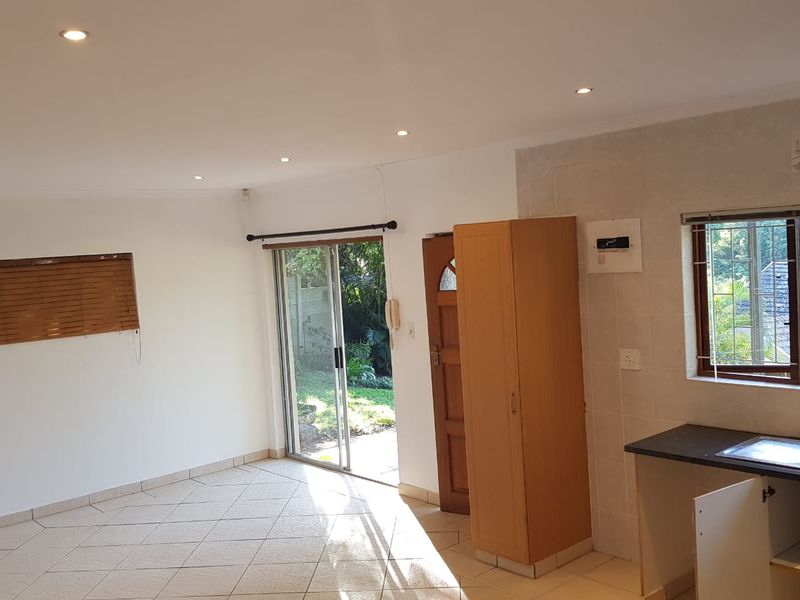 Open-plan living area featuring tiled floors, recessed lighting, and a functional kitchen space with direct access to the garden through a sliding door.