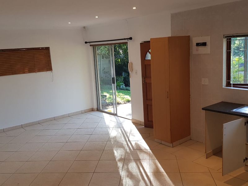 An open-plan living and kitchen area featuring tiled floors, recessed lighting, and direct access to the garden through a sliding glass door.