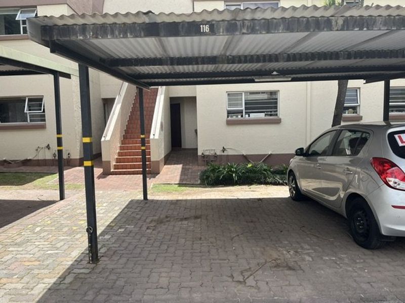 Exterior view of an apartment complex featuring a covered carport, paved driveway, and an external staircase leading to the unit entrance.