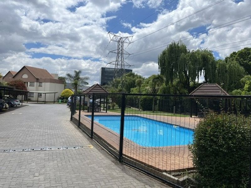 Communal swimming pool area featuring a paved surround, gazebo, and adjacent carport parking within the apartment complex grounds.