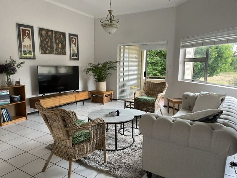 A bright living room featuring tiled flooring, a large window, and a sliding glass door providing access to the outdoor area.