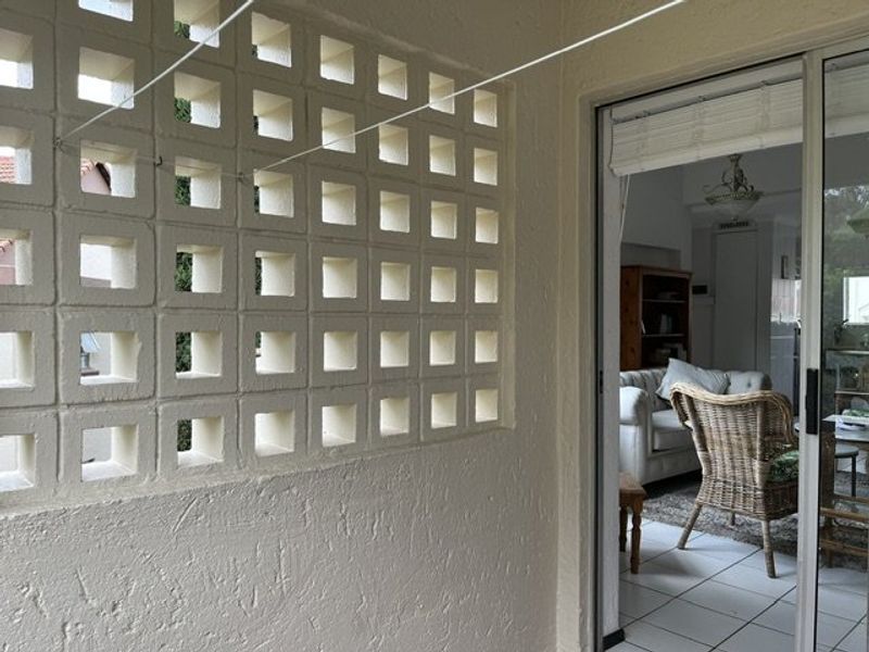 A covered balcony featuring a decorative breeze block screen wall and sliding glass door access to the interior living area.
