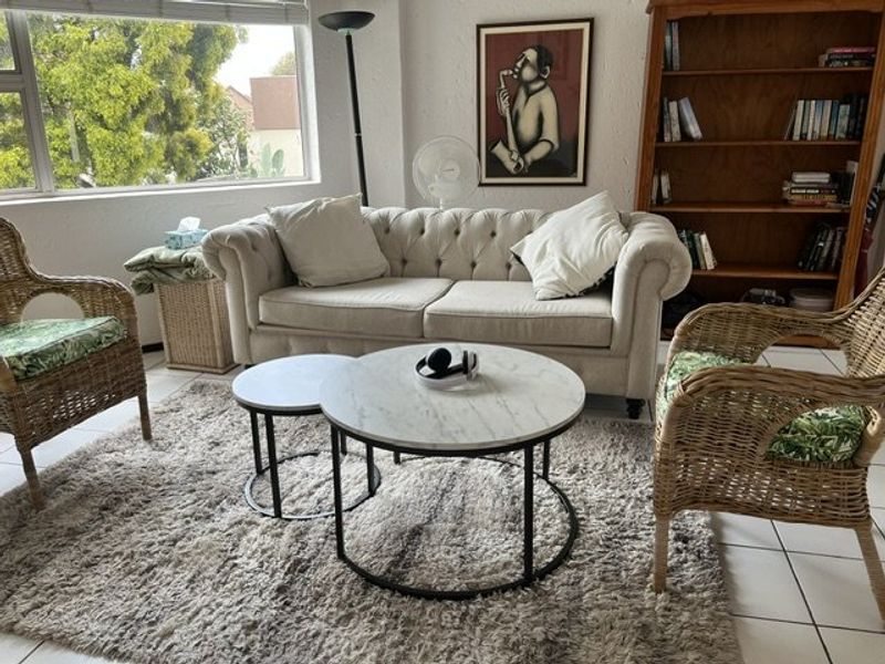 A bright living room featuring large windows that provide natural light and neutral tiled flooring throughout the space.