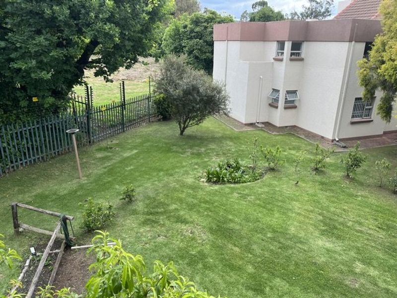 A view of the rear garden area featuring a lawn, established trees, and security fencing surrounding the property perimeter.