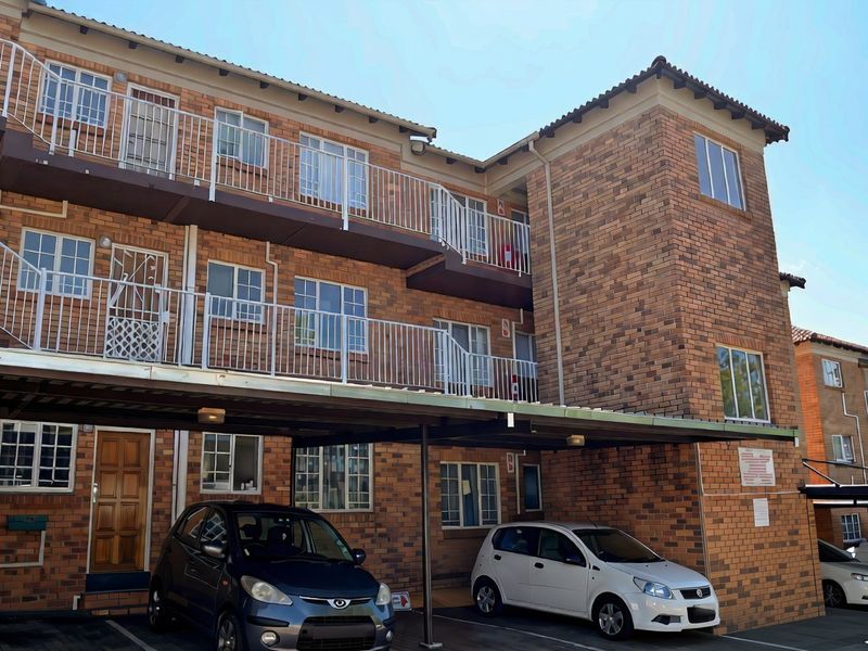 Exterior view of a multi-story face brick apartment building featuring covered parking bays and private balconies with metal railings.