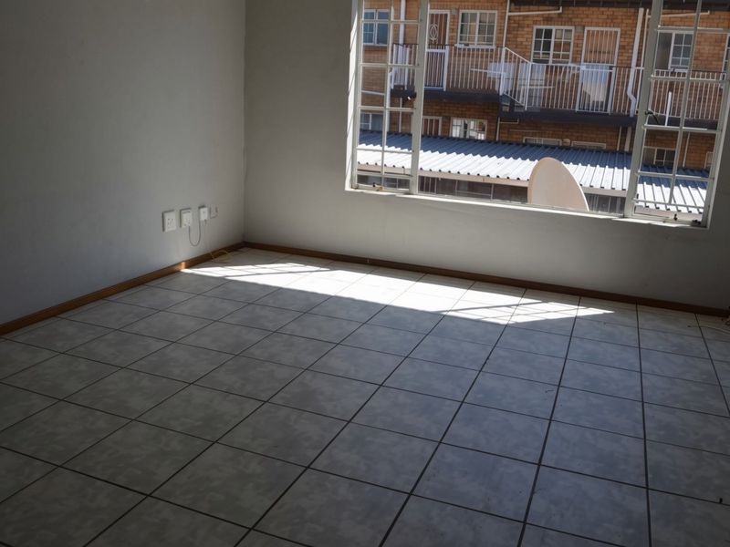 An empty living room featuring tiled flooring, large windows, and neutral walls, offering a blank canvas for personalization.