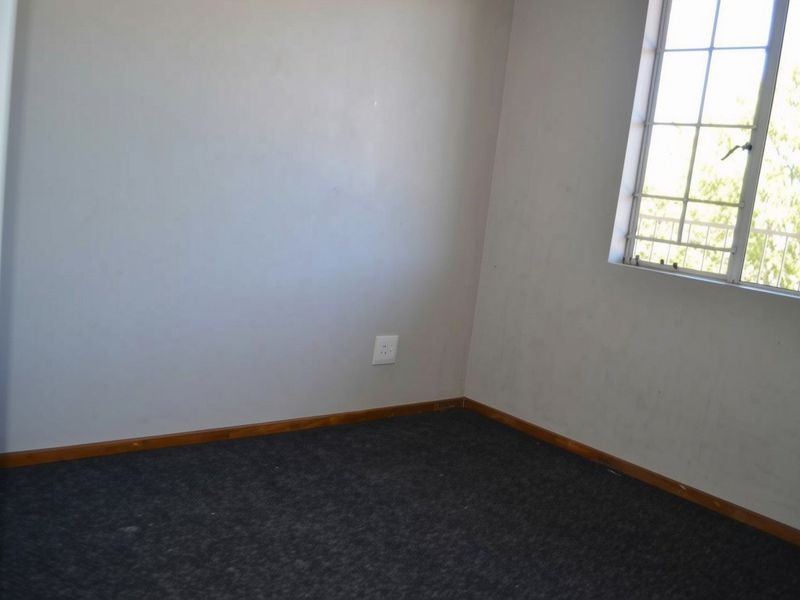 An empty bedroom featuring carpeted flooring, timber skirting boards, and a window fitted with security bars.