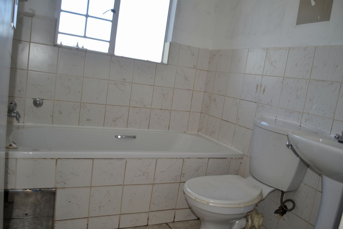 A dated bathroom featuring a bathtub, pedestal basin, and toilet with tiled walls, requiring cosmetic updates and repairs to finishes.