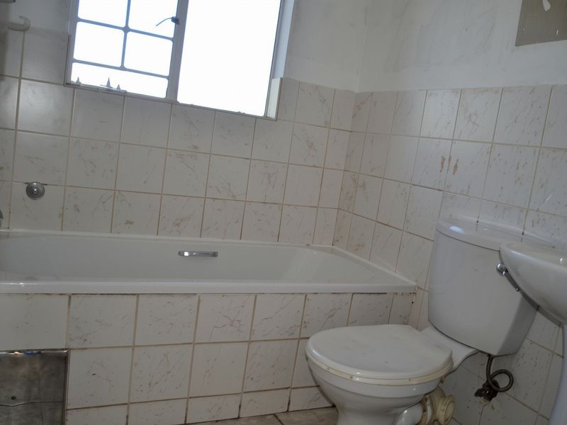 A dated bathroom featuring a bathtub, pedestal basin, and toilet with tiled walls, requiring cosmetic updates and repairs to finishes.