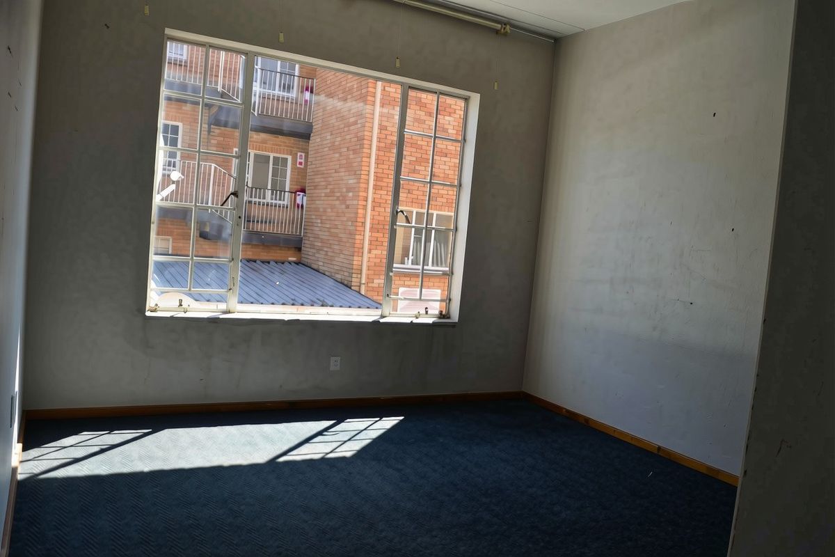 An empty bedroom featuring carpeted flooring and a large window with views of the adjacent building facade.