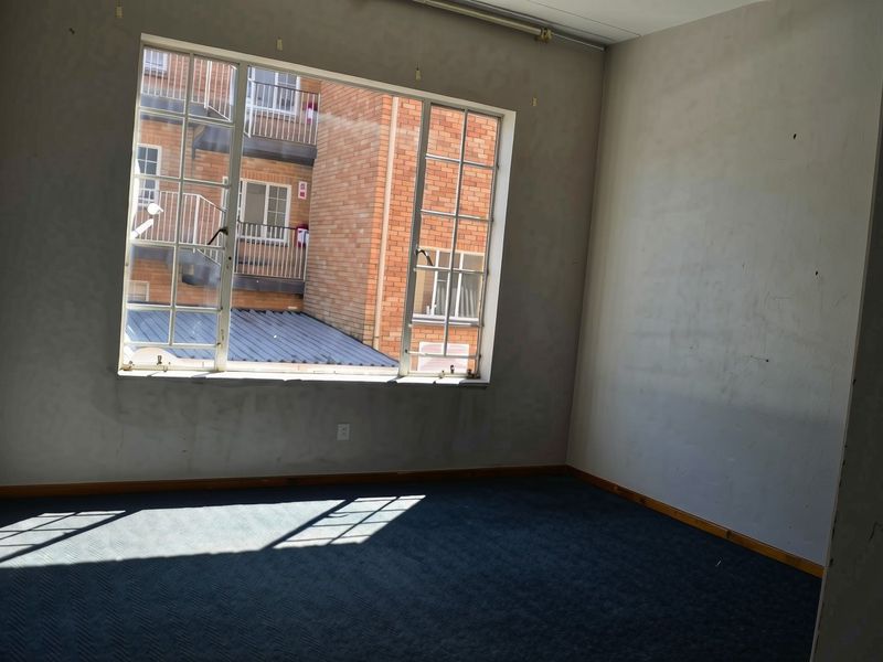 An empty bedroom featuring carpeted flooring and a large window with views of the adjacent building facade.