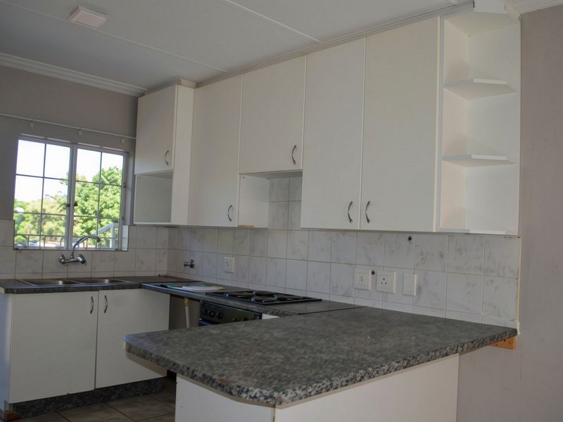 A functional kitchen featuring white cabinetry, laminate countertops, a built-in gas hob, and a tiled backsplash, offering a clean and practical workspace.