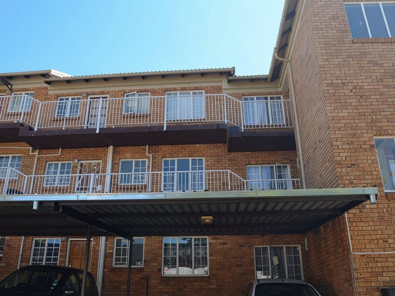 A multi-story apartment building facade featuring face brick construction, metal balcony railings, and a covered carport area.