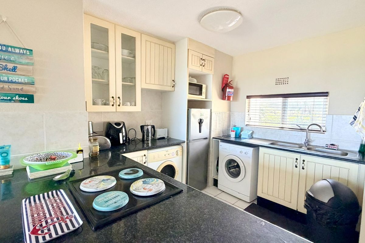 Functional kitchen featuring cream cabinetry, granite countertops, tiled backsplash, and integrated laundry facilities, offering a practical layout for daily use.