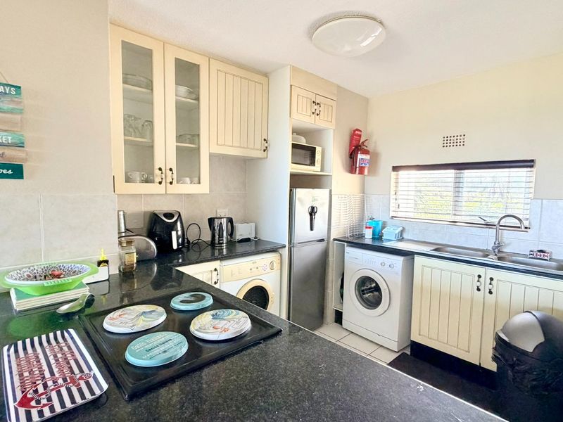 Functional kitchen featuring cream cabinetry, granite countertops, tiled backsplash, and integrated laundry facilities, offering a practical layout for daily use.