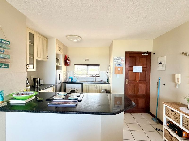 Open-plan kitchen area featuring granite countertops, built-in cabinetry, and tiled flooring, seamlessly connected to the main entrance of the apartment.
