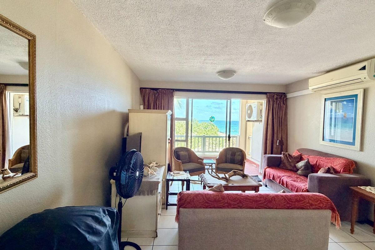 A comfortable living room featuring tiled floors, a split-system air conditioner, and large sliding glass doors that open to a balcony with ocean views.