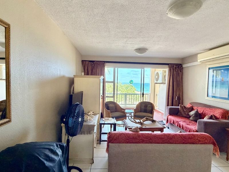 A comfortable living room featuring tiled floors, a split-system air conditioner, and large sliding glass doors that open to a balcony with ocean views.