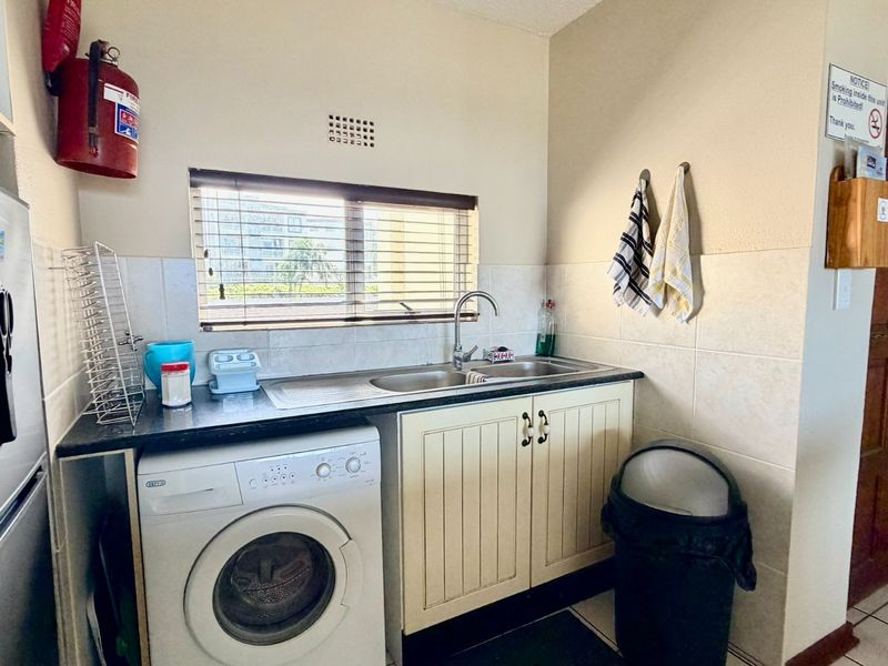A functional laundry area featuring a stainless steel sink, tiled splashback, and built-in cabinetry with space for a washing machine.